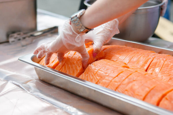 A cook is taking sliced salmon from the metal container