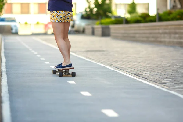 A woman in blue shirt and striped shorts is skateboarding