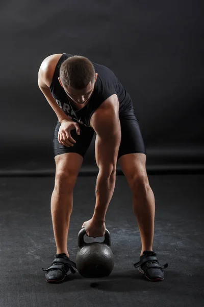 A male bodybuilder in black fitness clothes training with kettlebell