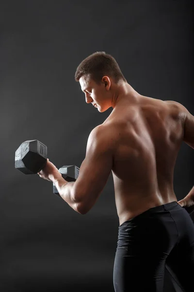 A portrait of bodybuilder in black fitness shorts posing with dumbbell