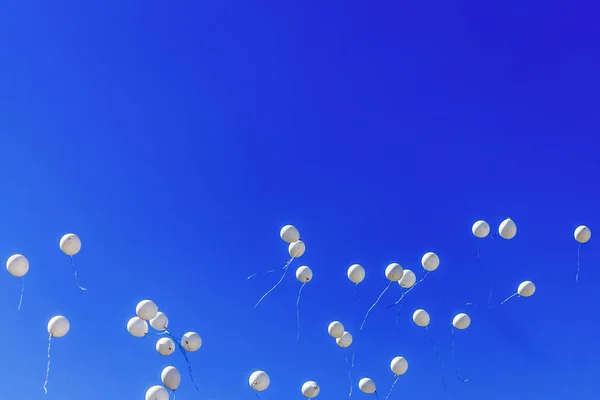 Bir sürü beyaz balonlar mavi gökyüzüne karşı uçuyor.
