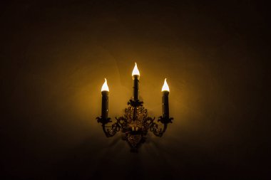 Arka plan için karanlık gölgeler sarı duvardaki geceleri üç mum ile altın elektrik şamdan.