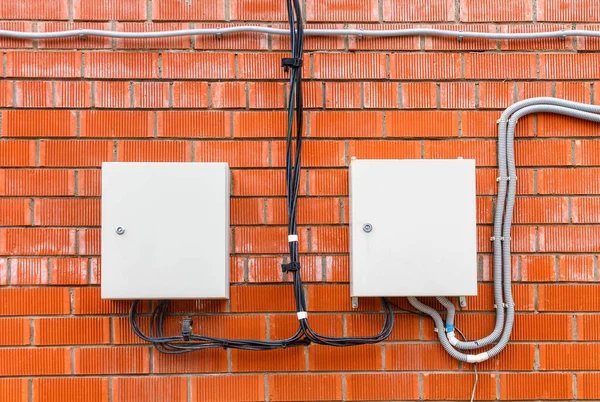 İki beyaz kutu kırmızı tuğla duvar bir elektrik yüksek gerilim kablosu ile. Ortasında siyah bir kablo ile bağlı.