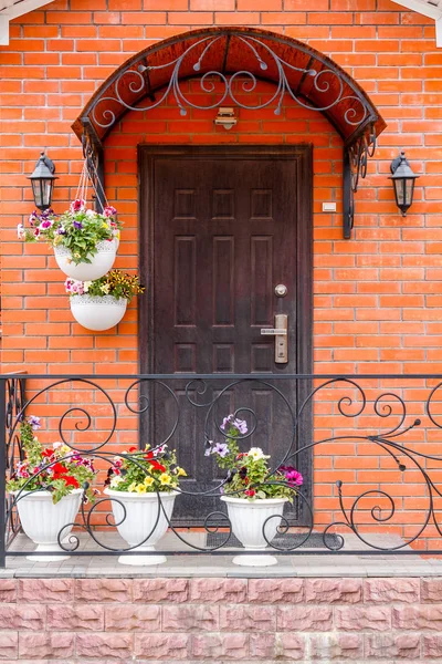 A beautiful porch in a rich house with black door, red brick wall and flower pots.