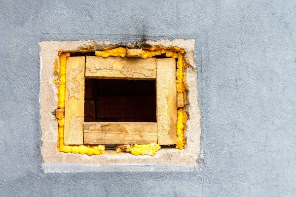 A square hole in a brick wall painted with gray paint.