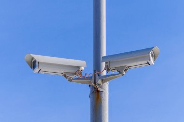 Mavi gökyüzüne karşı iki güvenlik kamera izleme.