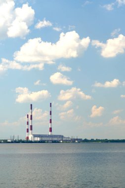 Beyaz bulutlar ile mavi bir gökyüzü altında büyük bir gölün kıyısında yüksek borular ile yoğuşma güç santrali. Ekoloji ve enerji.