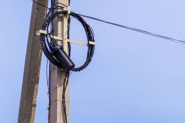 An internet or electric cable, rolled up into a ring, hangs on a pole. City landscape.