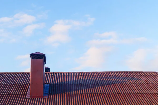 Chimney on the red roof of the house against the blue sky. City exterior.