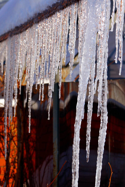 Many large and sharp icicles hang on the roof of the house. Seasons.