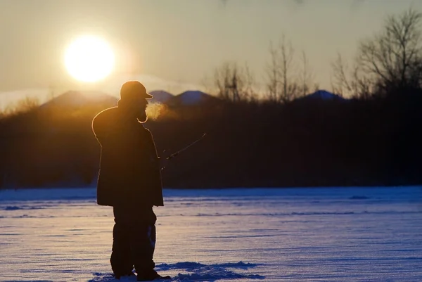 Рыбак на закате зимой — стоковое фото