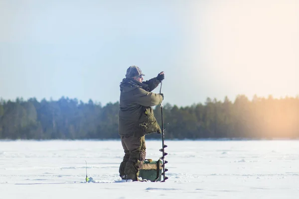 冬の釣りドリル穴の氷のドリルの男 — ストック写真