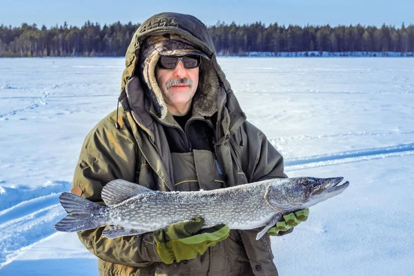 Male fisherman with a mustache in sunglasses is holding a big fish pike in the winter — Stock Photo, Image