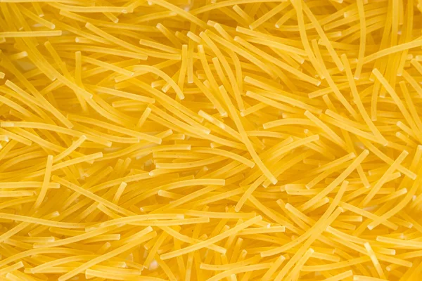 Krátké tenké vermicelli na celém pozadí. textura suchých žlutých těstovin. — Stock fotografie