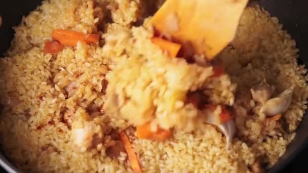 Cooking pilaf close-up. Cook mixing rice, garlic pork and sliced carrot. Process of pilaf cooking. — Stock Video