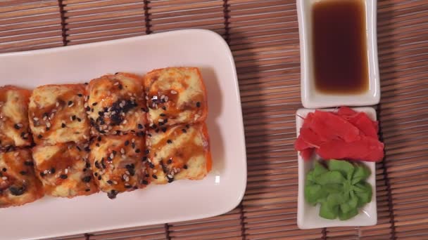 Sabrosos rollos de sushi sobre tabla de madera con salsa de soja, jengibre, wasabi en bambú decorativo — Vídeo de stock