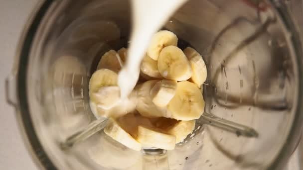 Cozinhando batidos de banana em um liquidificador. fatias de banana na vista superior do leite — Vídeo de Stock