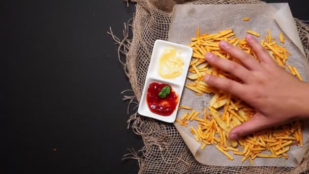 Ketçap ve peynir soslu siyah arkaplanlı beyaz bir kağıtta patates kızartması. Üst manzara, abur cubur yemek. — Stok video