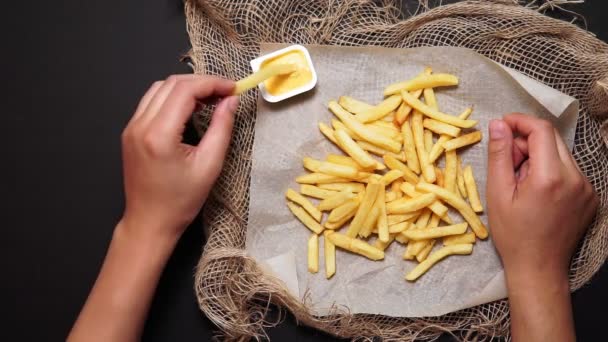 Hombre come papas fritas con salsa de queso en una mesa oscura, vista superior. plano laico — Vídeo de stock