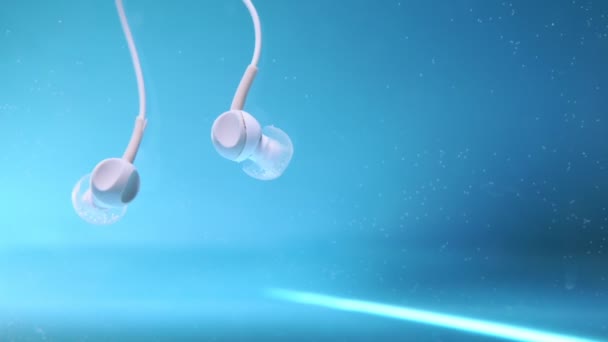 Auriculares bajo el agua sobre fondo azul. Escuchar música, accesorio impermeable — Vídeos de Stock