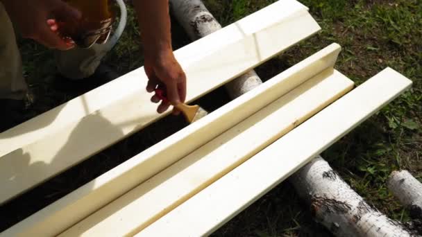 Mano dell'uomo che tiene una spazzola applicando vernice su una superficie di legno. Ripristinare tavole di legno. — Video Stock