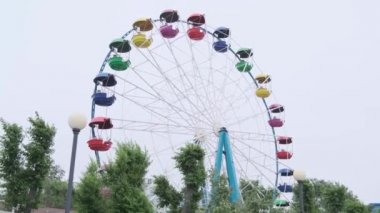 Güçlü rüzgar nedeniyle onu ağaçlar sallanan önünde insanlar olmadan iplik oturma için renkli kabinleri ile beyaz demir dönme dolabı ve beyaz bir sokak lambası