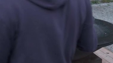 uzun kollu ve bir başlık ile koyu bir ceket bir adam dikkatle bir defada kıyılmış odun bir koyar, böylece yakmak için değil, erimiş yuvarlak şekli altında yuvarlak demir Barbekü, ve üst bir yuvarlak ızgara. sahne eylemleri Vladivostok Rusya.