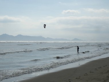 Bir adam kitesurf yapıyor, diğeri kıyıda duruyor.
