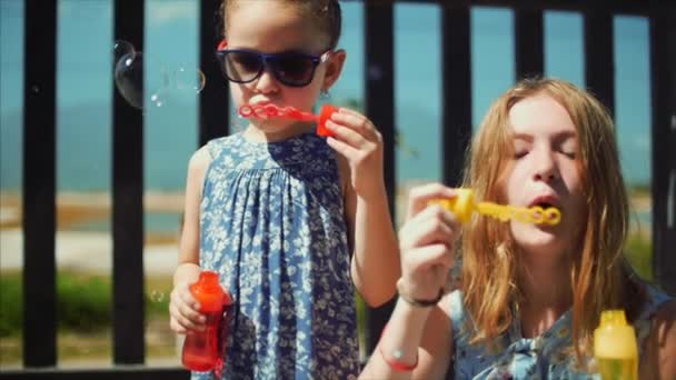 Feliz família sorridente, irmãs estão brincando, soprando bolhas de sabão no verão ao ar livre. Filmagem de stock . — Vídeo de Stock