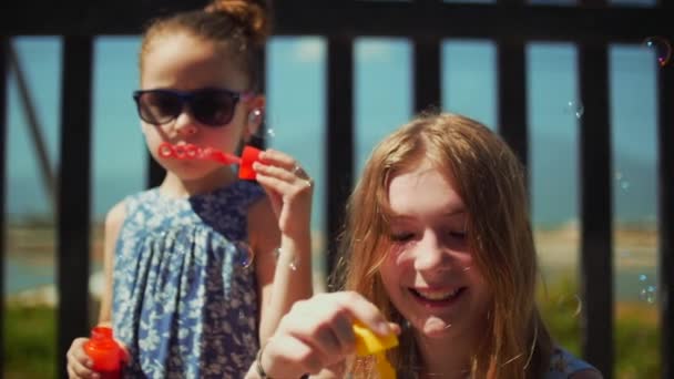 Feliz família sorridente, irmãs estão brincando, soprando bolhas de sabão no verão ao ar livre. Filmagem de stock . — Vídeo de Stock