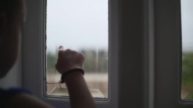 Yağmurda pencerenin dışındaki küçük kız bakar, küçük bir kız camda çizer.