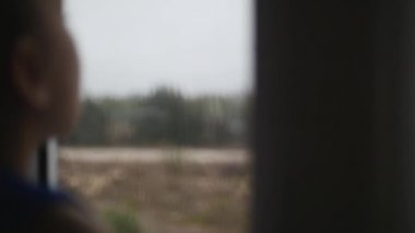 Yağmurda pencerenin dışındaki küçük kız bakar, küçük bir kız camda çizer.