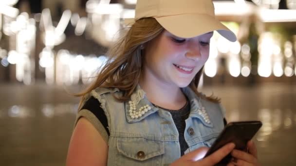 Atractiva adolescente usando un teléfono móvil mientras camina por las calles en una ciudad nocturna, en la ciudad nocturna de fondo. Material de archivo . — Vídeos de Stock