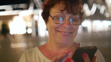 Bir gece şehirde arka plan gece şehrin sokaklarında yürürken bir cep telefonu kullanarak çekici kadın. Stok görüntüleri.