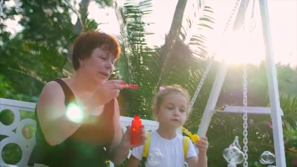 Glada leende familj, Mormor med barnbarn spelar, blåser såpbubblor i sommaren utomhus. Arkivfilmer. Slow motion. — Stockvideo