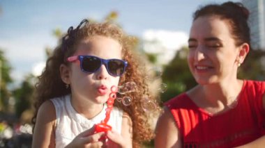 Mutlu anne ve çocuk parkında sabun köpüğü üfleme. Ağır çekim. Stok görüntüleri. Ağır çekim