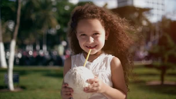Baba kaukázusi, kis lány, göndör haj, fehér ruha, ivás kókusz. — Stock videók