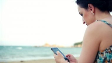 Deniz kenarında Smartphone kullanan genç beyaz kadın.
