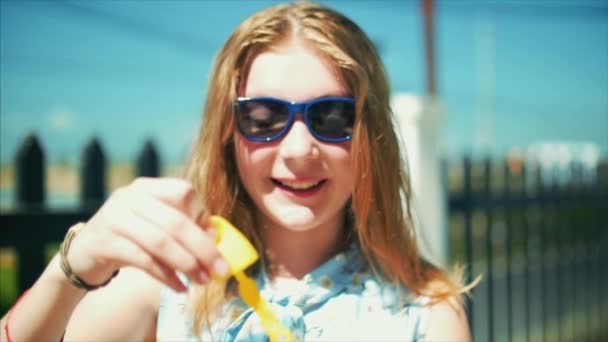 ハッピー 10 代の少女の白人の姿に笑みを浮かべて、カメラを見て笑みを浮かべて真夏の野外でシャボン玉を吹いています。クローズ アップ。映像素材集. — ストック動画