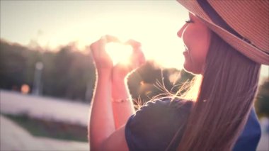 Eller güzel kadın ile kalp şekil verme gün batımı kız aşk sembolü jest turuncu güneş parlama ile gidiyor.