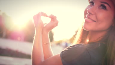 Eller güzel kadın ile kalp şekil verme gün batımı kız aşk sembolü jest turuncu güneş parlama ile gidiyor.