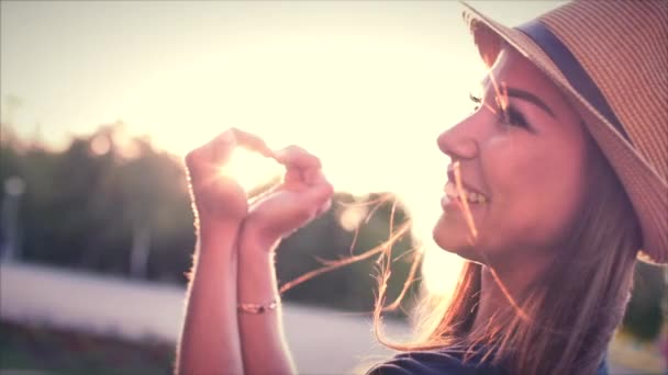 Belle femme faisant forme de coeur avec les mains au coucher du soleil Fille tenant geste de symbole d'amour avec fusée éclairante orange .