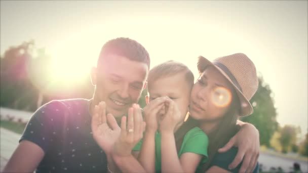 Familia feliz, madre feliz, padre feliz y el niño están sentados en la hierba, producir la figura de las manos del corazón . — Vídeo de stock