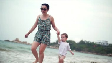 Genç aile, anne ve çocuk sahil boyunca yürüyor. Mutlu aile deniz kıyısında yürüyüş.