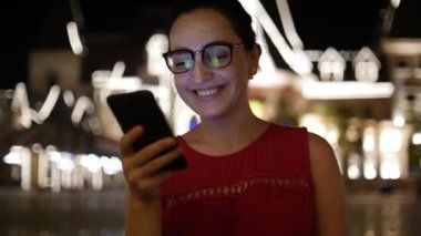 Çekici kız bir gece şehirde arka plan gece şehrin sokaklarında yürürken bir cep telefonu kullanarak. Stok görüntüleri.