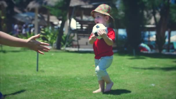 Schattige kleine jongen spelen met een voetbal loopt naar zijn moeder in een knuffel. Beeldmateriaal. — Stockvideo