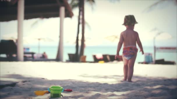 Menino de dois anos de idade caminha na praia de areia de verão nos trópicos ao longo da areia. Movimento lento . — Vídeo de Stock