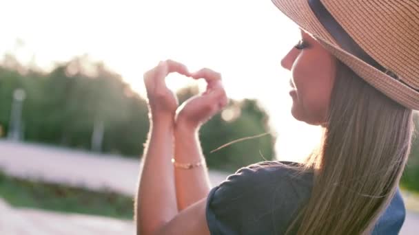 Όμορφη γυναίκα κάνοντας καρδιά σχήμα με τα χέρια στο ηλιοβασίλεμα κορίτσι κρατά ψηλά αγάπη σύμβολο χειρονομία με πορτοκαλί ήλιος φωτοβολίδα. — Αρχείο Βίντεο