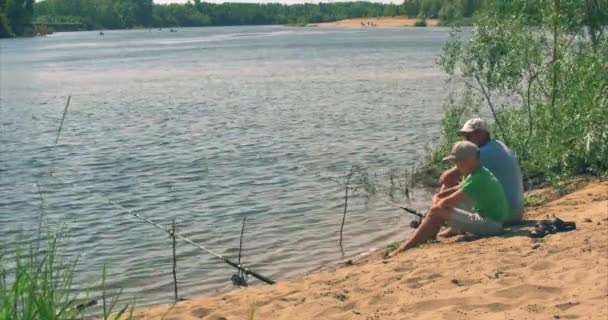 Feliz padre e hijo están sentados en la orilla del río, la pesca, papá e hijo están pescando en la mañana. Familia feliz . — Vídeos de Stock