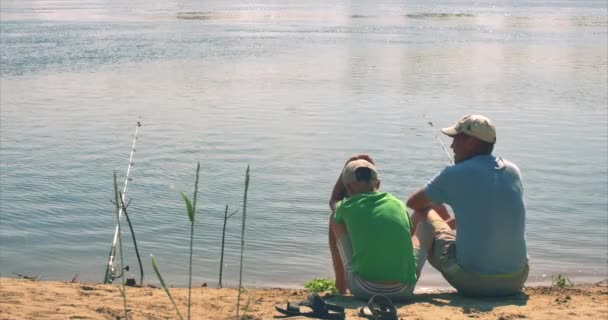 Mutlu baba ve oğul nehir kıyısında oturuyor, sabah balıkçılık balıkçılık, baba ve oğlu. Mutlu bir aile. — Stok video